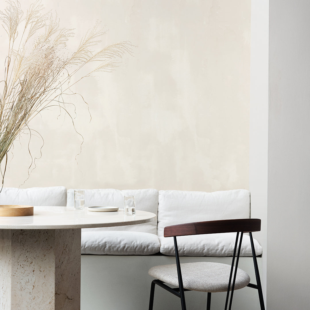 "Neutral beige wall with soft white cushions, minimalist round table, and sleek black chair, creating a serene aesthetic."