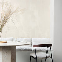 "Neutral beige wall with soft white cushions, minimalist round table, and sleek black chair, creating a serene aesthetic."
