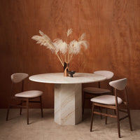 Round marble dining table with beige and cream tones, featuring soft pink upholstered chairs and a warm wooden backdrop.