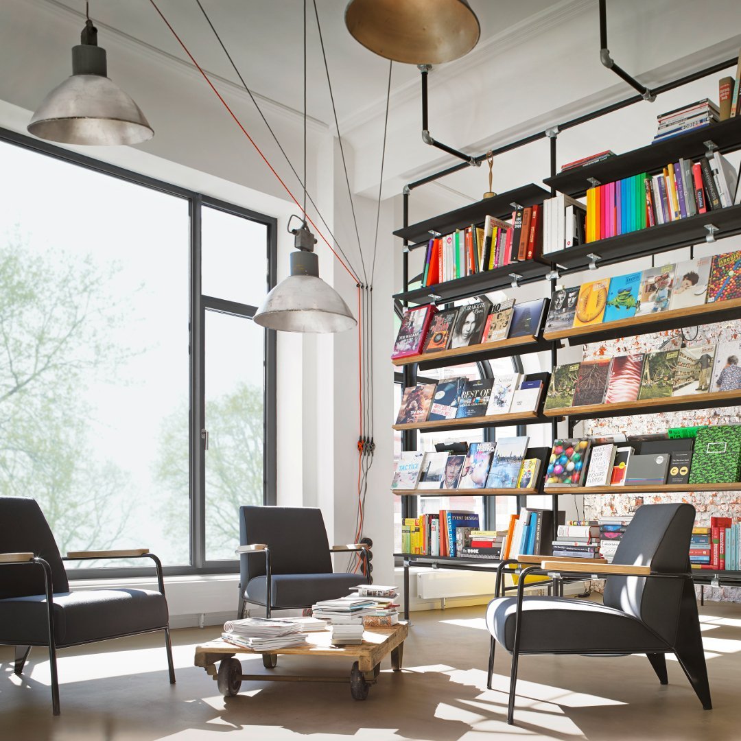 Modern eclectic seating area with black chairs, vibrant book spines, and natural light streaming through large windows.