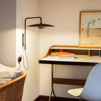 Modern workspace with warm wooden tones, sleek black light fixture, and colorful accents on desk, featuring minimalistic design.