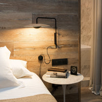 Stylish bedside setup with warm wood tones, sleek black lamp, and soft white bedding. Elegant marble table adds contrast.