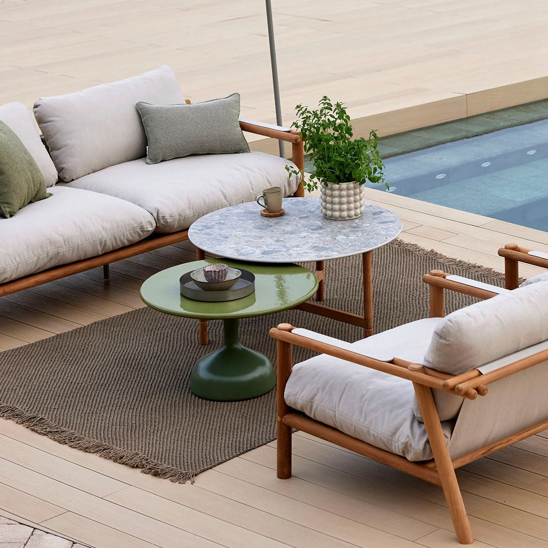 Cozy outdoor seating with beige cushions, green accent table, gray marble top, and neutral woven rug.