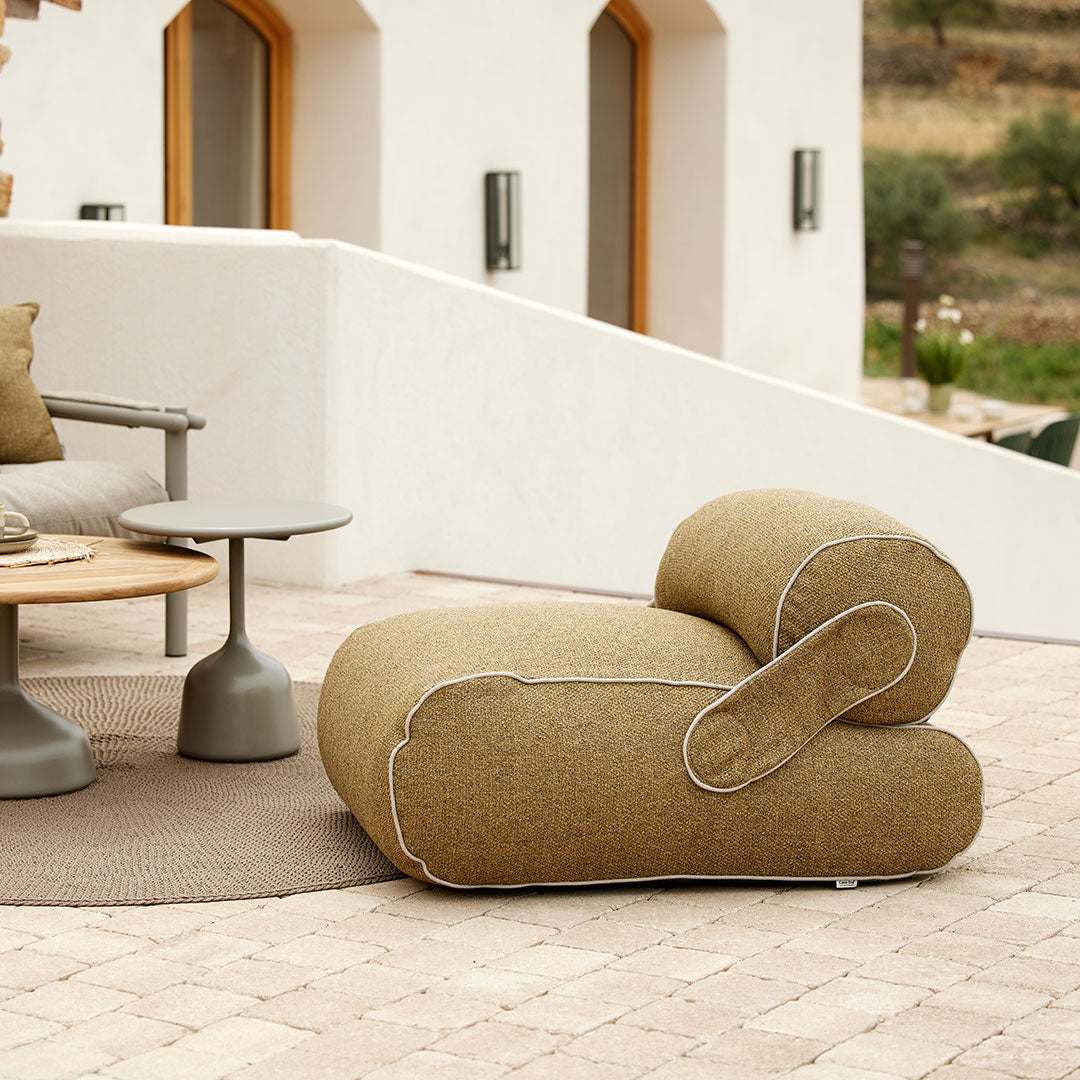 "Curved beige lounge chair with a textured fabric and contrasting white stitching, set against modern outdoor decor."