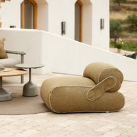 "Curved beige lounge chair with a textured fabric and contrasting white stitching, set against modern outdoor decor."