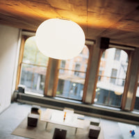 Modern white orb ceiling lamp against a warm wooden ceiling, casting a soft glow in a stylish, minimalist space.