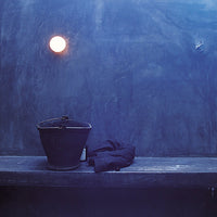 "Deep blue wall, round light fixture, black bucket, and dark cloth create a minimalist, modern aesthetic."