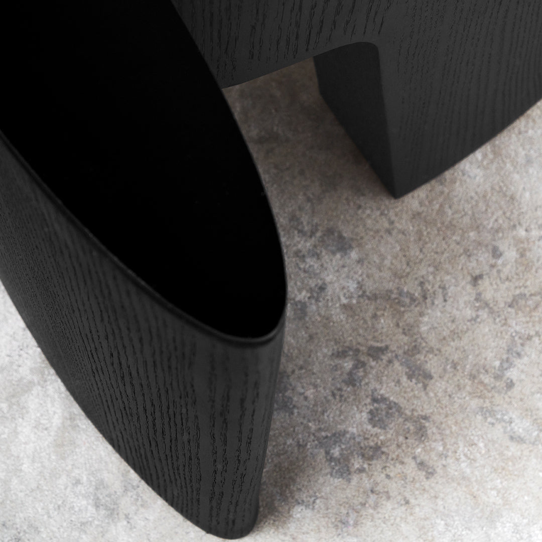 Black curved wood structure with a smooth finish against a textured gray background.