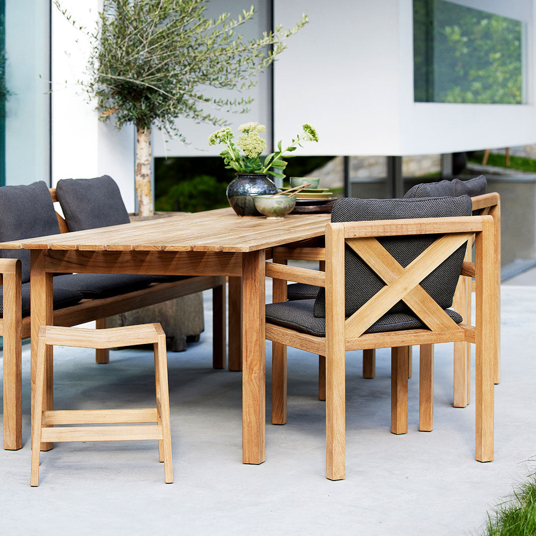 "Natural wood dining table with gray cushions and modern cross-back chairs, featuring earthy tones and minimalist design."