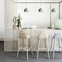 Light wood cabinetry, pale gray and beige bar stools, and green pendant lights create a fresh, modern aesthetic.