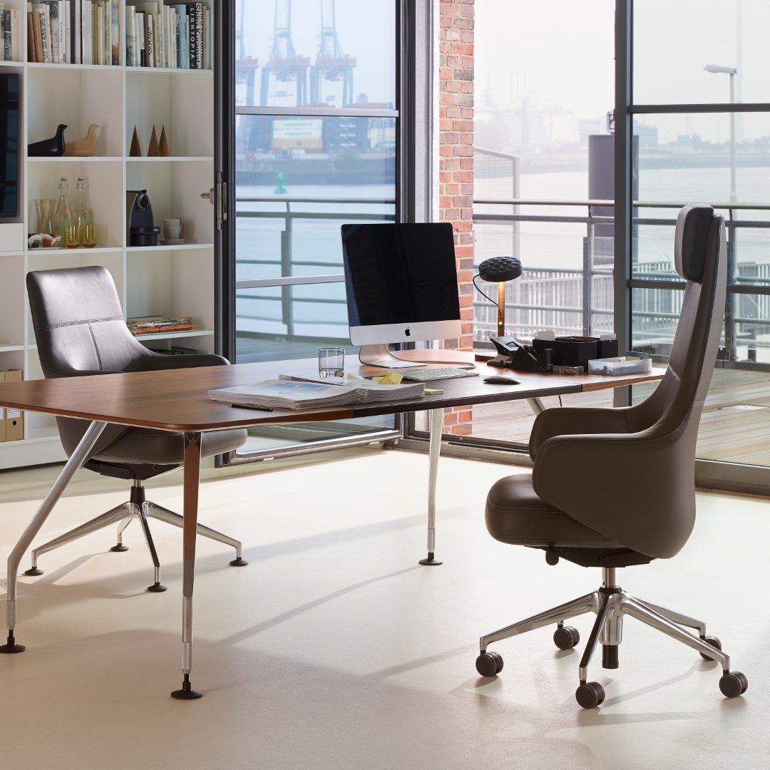Modern office with sleek black and gray chairs, a wooden desk, and city skyline views through large windows.