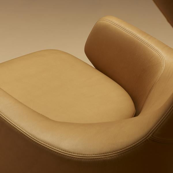 Tan leather armchair with smooth texture and minimalist design, featuring subtle curves and contemporary style.