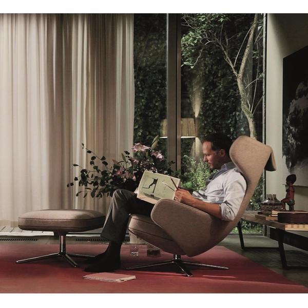 "Modern beige armchair with smooth upholstery, paired with a round ottoman on a vibrant red carpet."