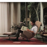 "Modern beige armchair with smooth upholstery, paired with a round ottoman on a vibrant red carpet."
