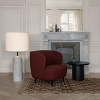Cozy maroon chair, grey marble lamp, black round table, and patterned brown and cream rug in a chic interior.