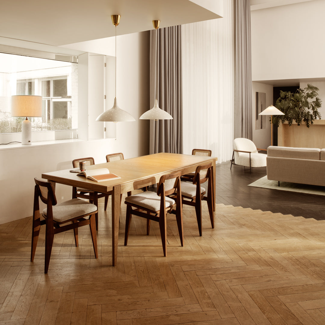 Modern dining room with wood table, mid-century chairs, gray curtains, and light wood herringbone flooring.