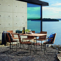 Outdoor dining set with wooden slatted chairs, neutral tones, and colorful patterned cushions against a serene lakeside backdrop.
