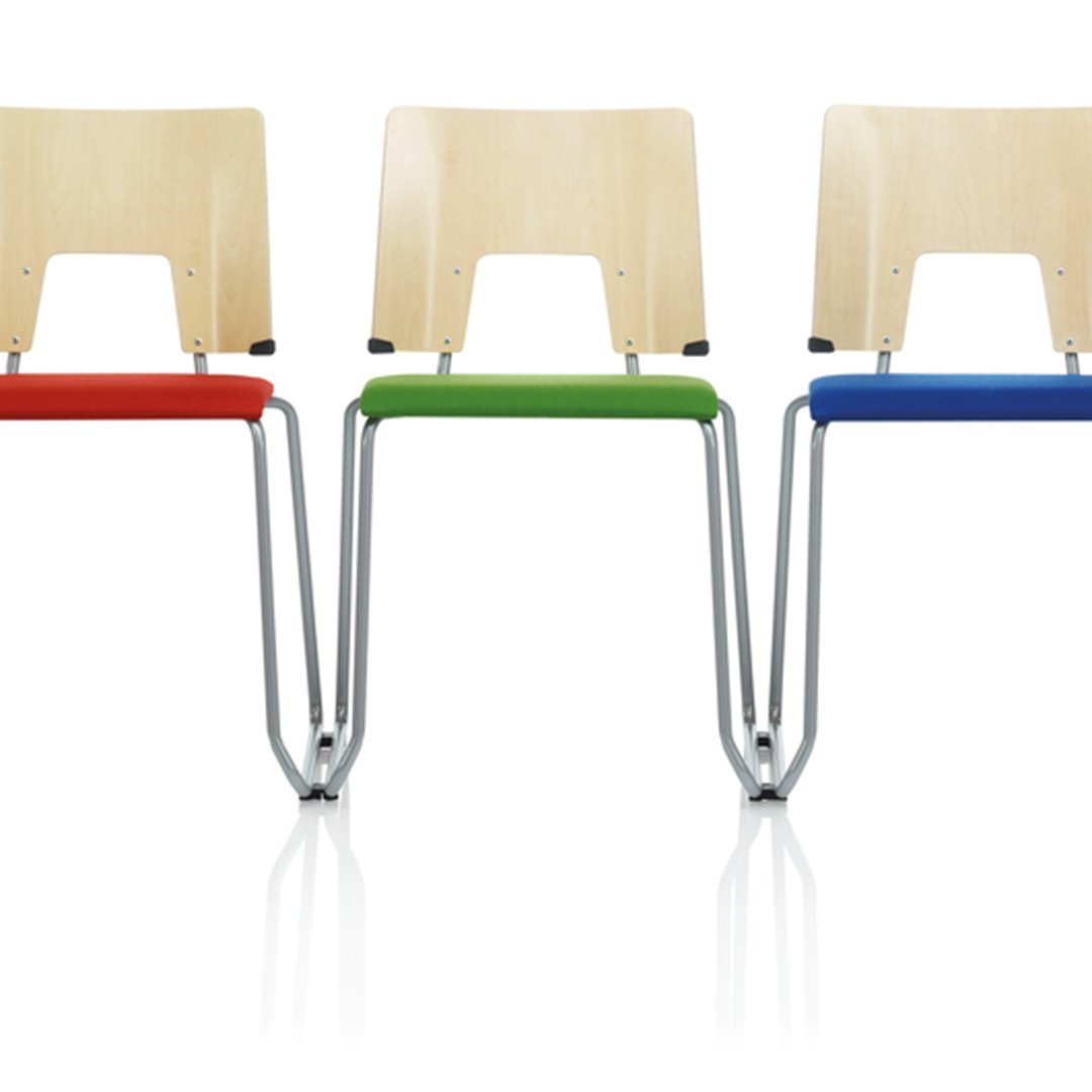 Three modern chairs with natural wood seats and vibrant red, green, and blue padded cushions. Sleek silver metal frames.
