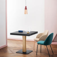 Modern black tabletop with natural wood base; soft pastel pink wall; teal and beige chairs, creating a stylish contrast.
