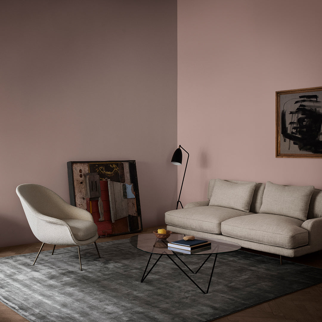 Minimalist living room featuring a light pink wall, gray rug, white sofa, and modern decor for a cozy ambiance.