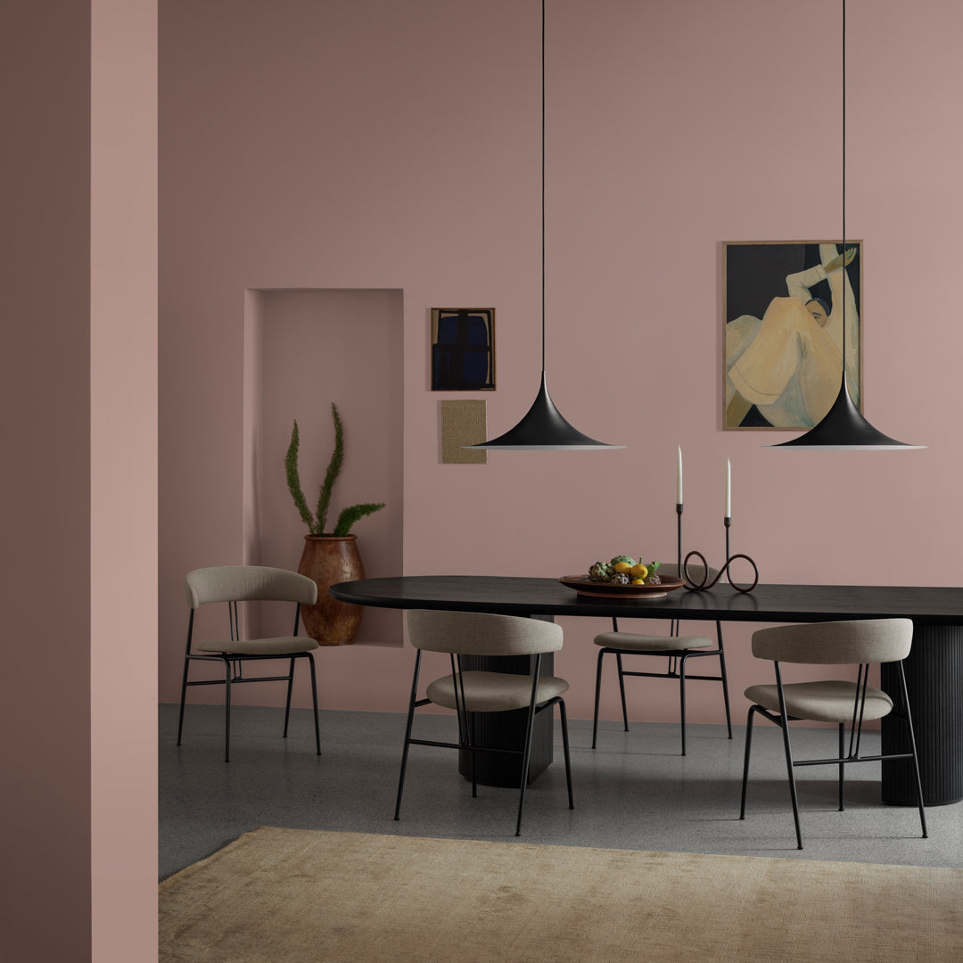 Modern dining room featuring soft pink walls, black table, and minimalist decor with earth tones and elegant lines.