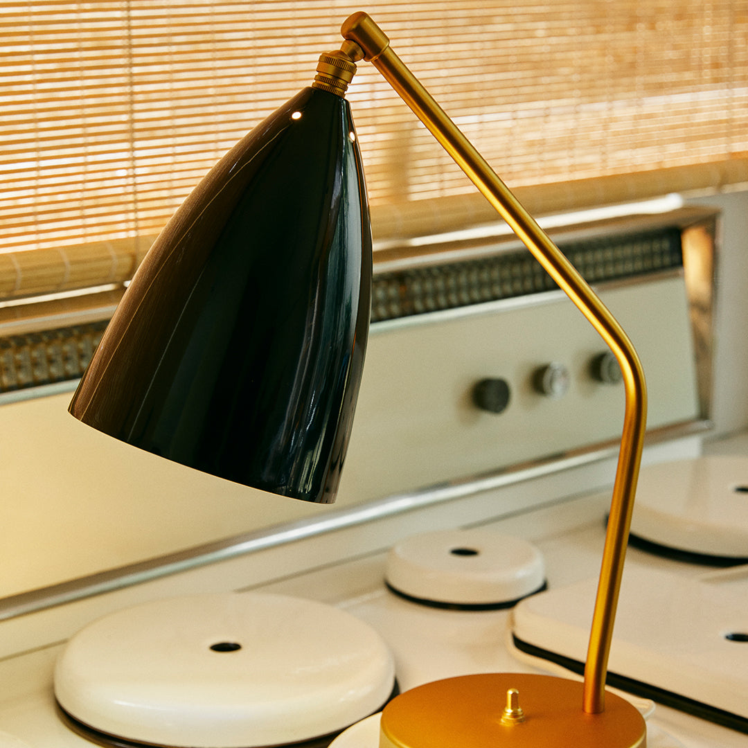 Black cone lampshade with a gold arm and base, set against a light wooden backdrop. Elegant modern design.