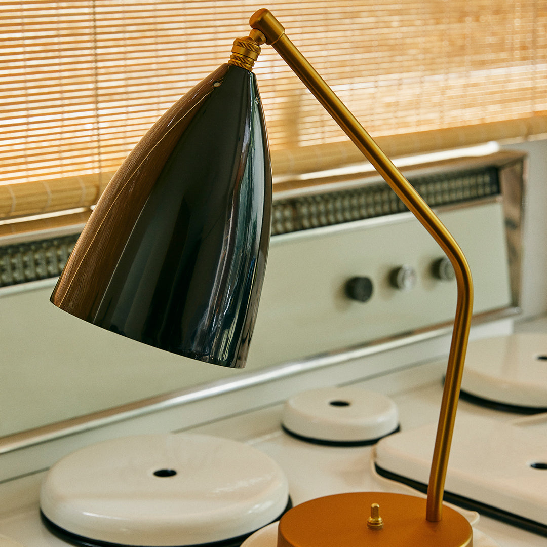 Modern black and gold desk lamp with a sleek cone shade, set against a light wood backdrop. Stylish and minimalist design.