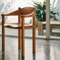 Natural wood chair with smooth curved design, showcased against a minimalist interior and lush green plants.