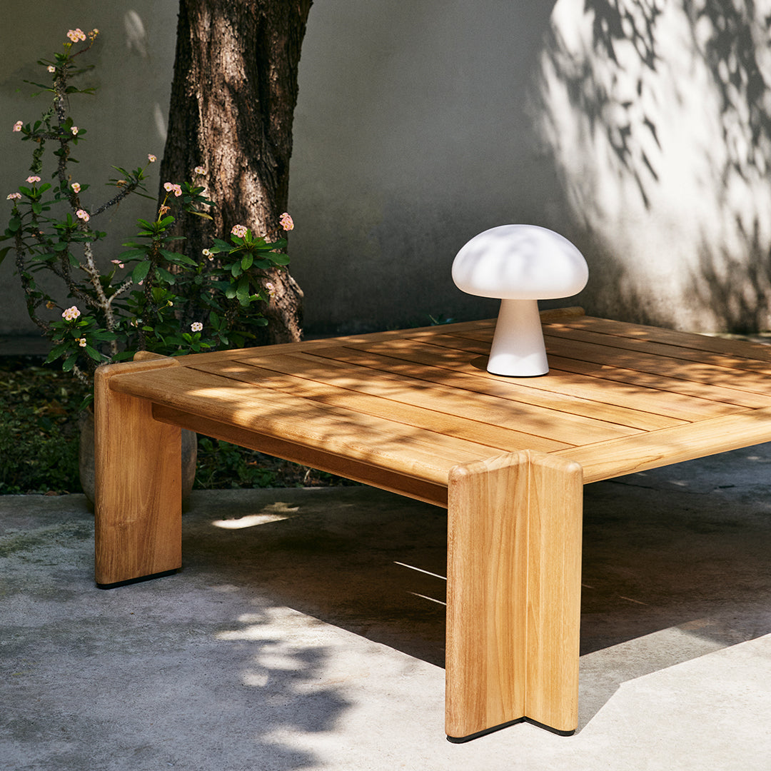 Natural wood coffee table with a smooth finish, complemented by a white mushroom-shaped lamp.