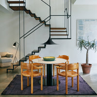 Modern dining set featuring warm wooden chairs, a sleek black table, and a rich purple rug in a stylish room setting.