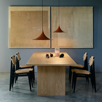 Scandinavian dining table with light wood finish, black chairs, and warm-toned pendant lights against neutral-toned artwork.