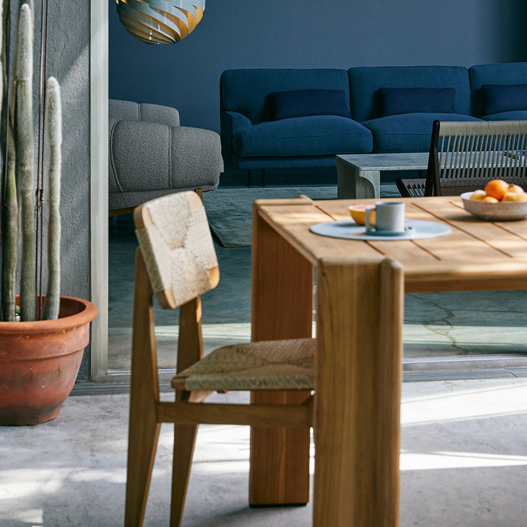 Natural wood table with beige woven chair, set against blue and gray accents in a modern living space.