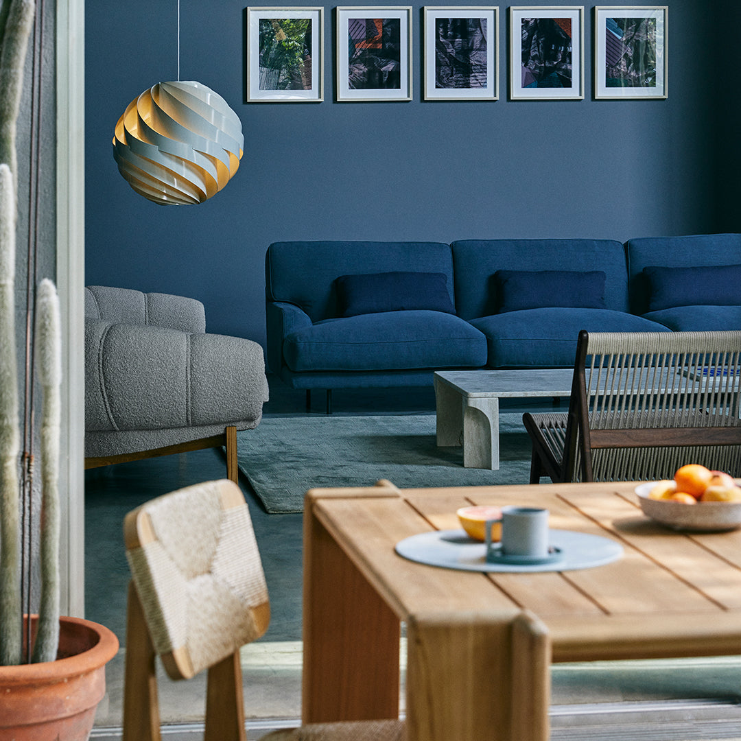 Elegant blue sofa set against a dark blue wall, paired with light wood furniture and soft neutrals. Modern decor accents.