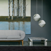 Gray sofa with light wood legs, marble table, and textured pendant lights against a dark wall and serene landscape painting.