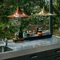 Orange and yellow pendant lamps above a sleek countertop, surrounded by greenery and colorful kitchenware.
