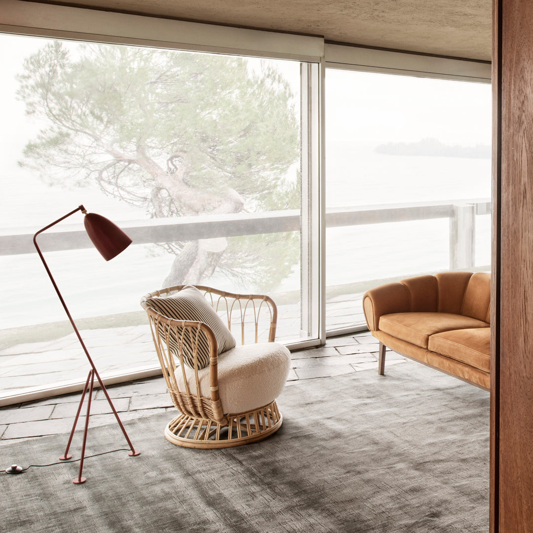 Bohemian rattan chair with white cushion, warm brown sofa, and modern red lamp, set in a light, airy room.