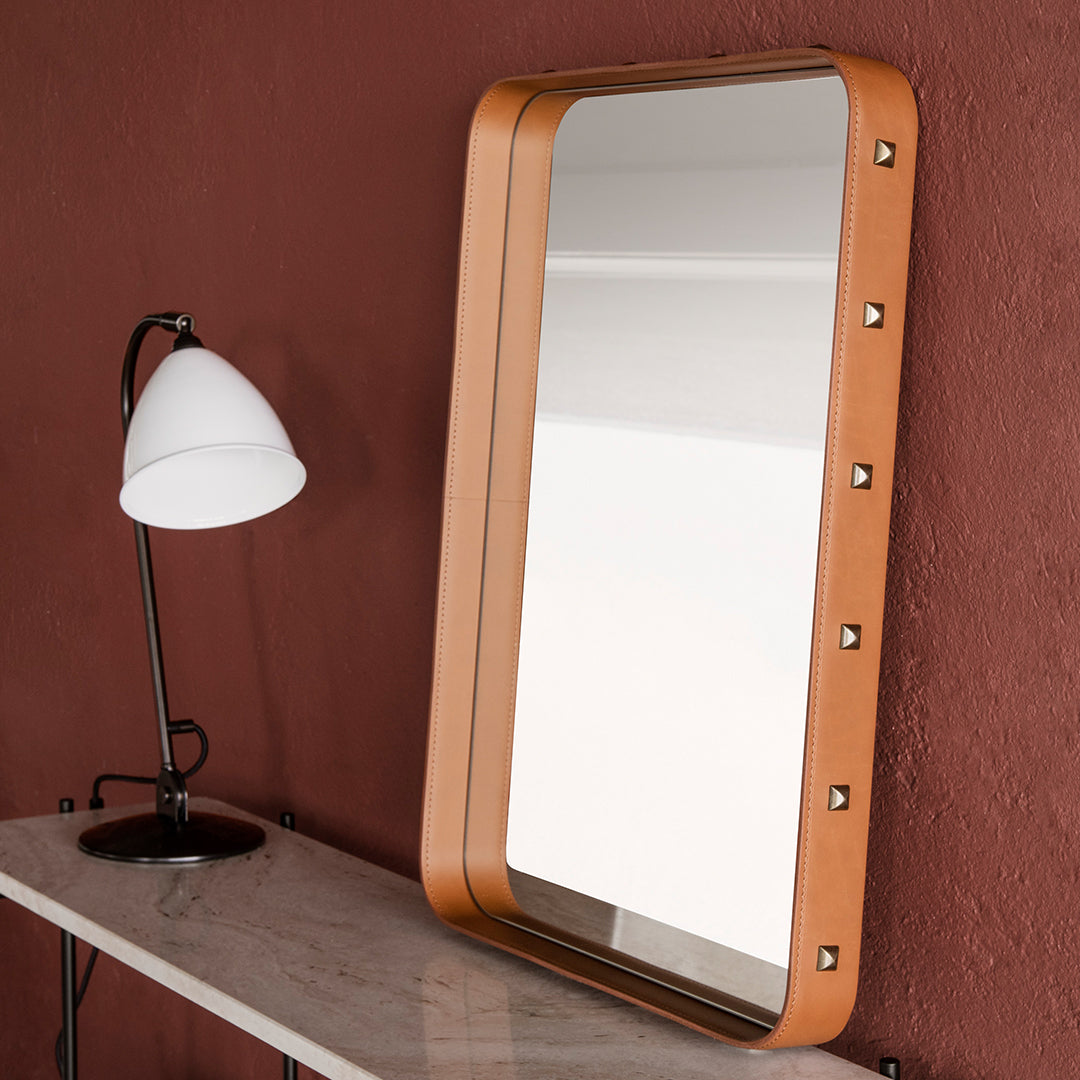 "Rectangular mirror with a warm tan frame and subtle silver accents against a reddish wall backdrop."