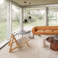 "Modern living room with a mustard sofa, wooden chair, and neutral-colored furnishings against a green outdoor backdrop."