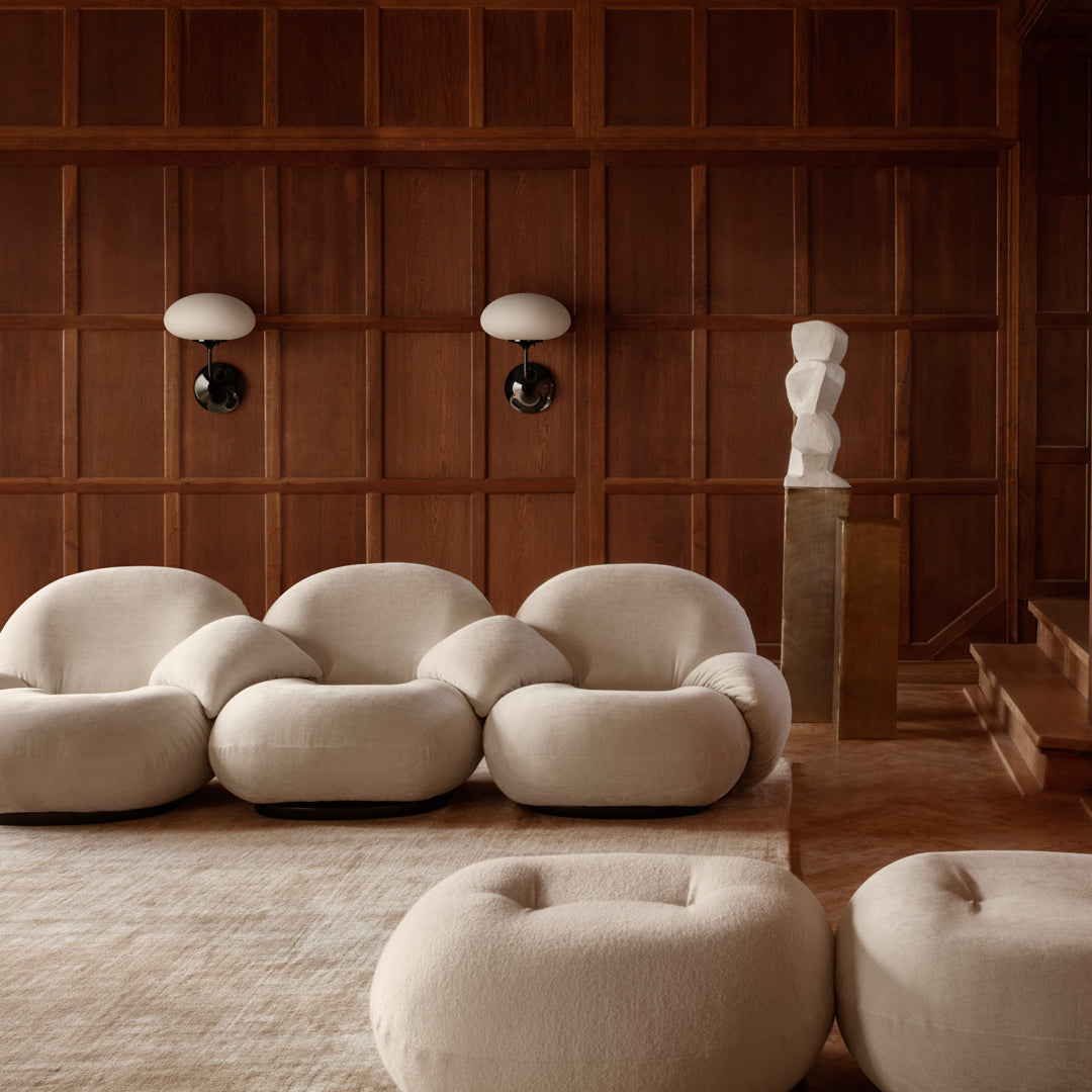 Soft beige sofa with rounded shapes in a warm, wooden interior. Complemented by a textured, light area rug.
