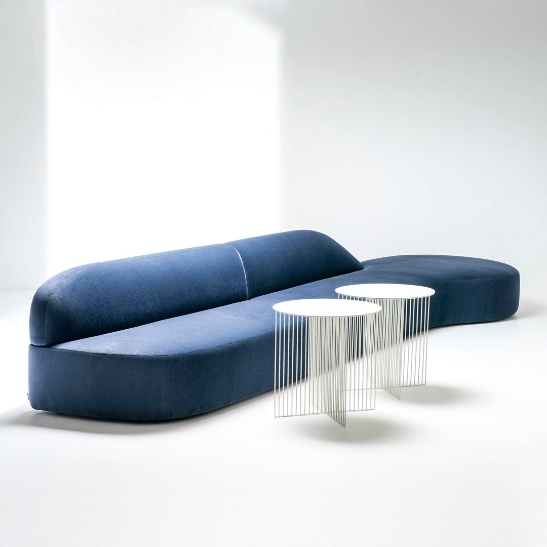 Elegant blue curved sofa with smooth fabric texture paired with two minimalist white side tables.