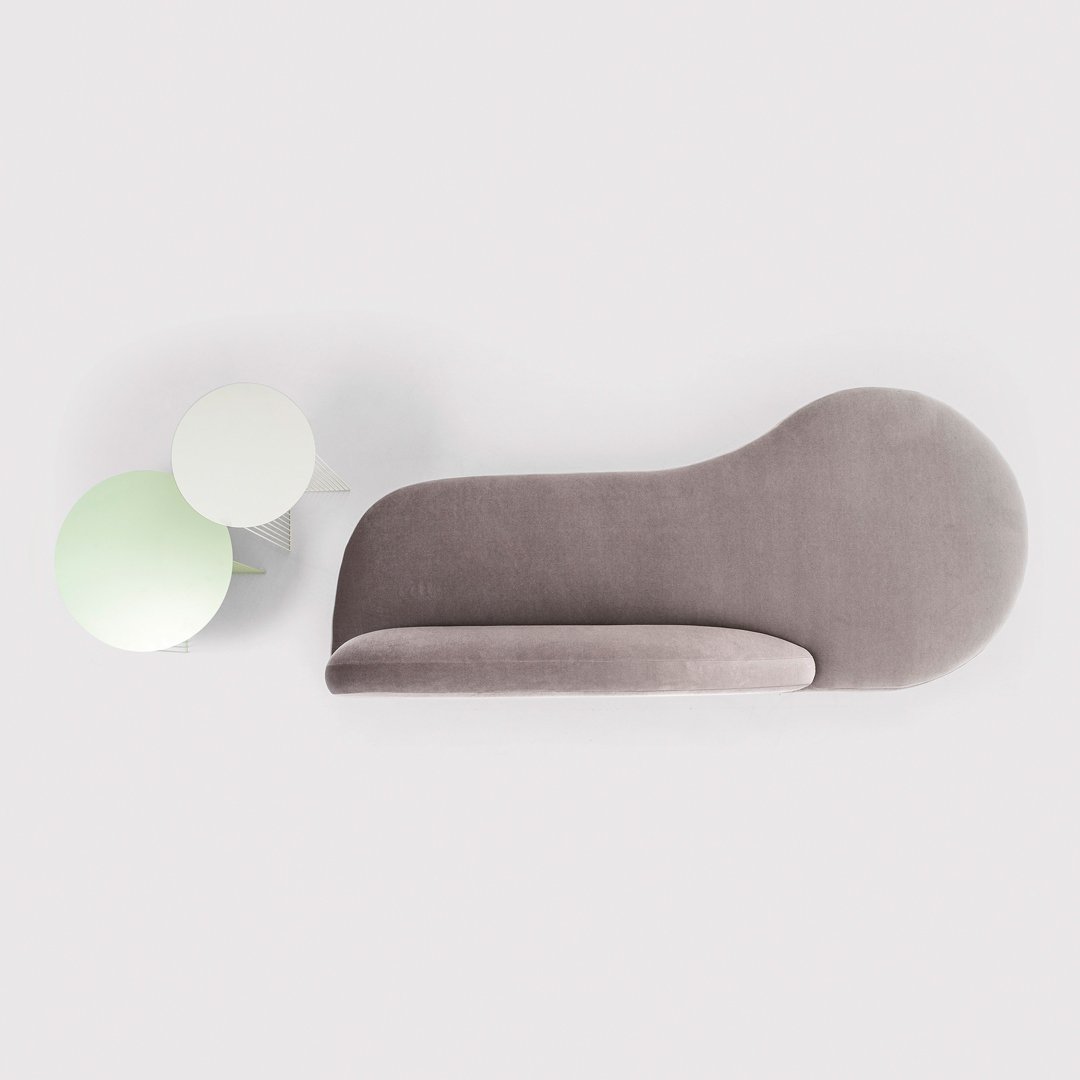 Gray curved sofa with smooth texture, paired with round green and white side tables, minimalist modern style.