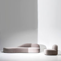 Stylish soft pink curved sofa and matching chair against a minimalistic gray background. Modern, elegant design.