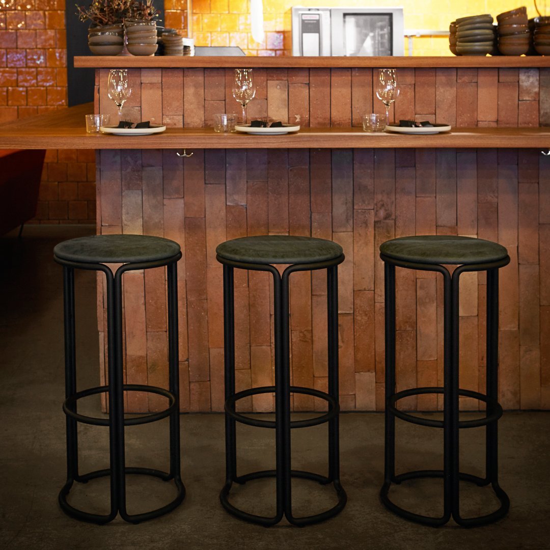 Set of three black metal bar stools with round seats, featuring a sleek minimalist design against a warm wood backdrop.