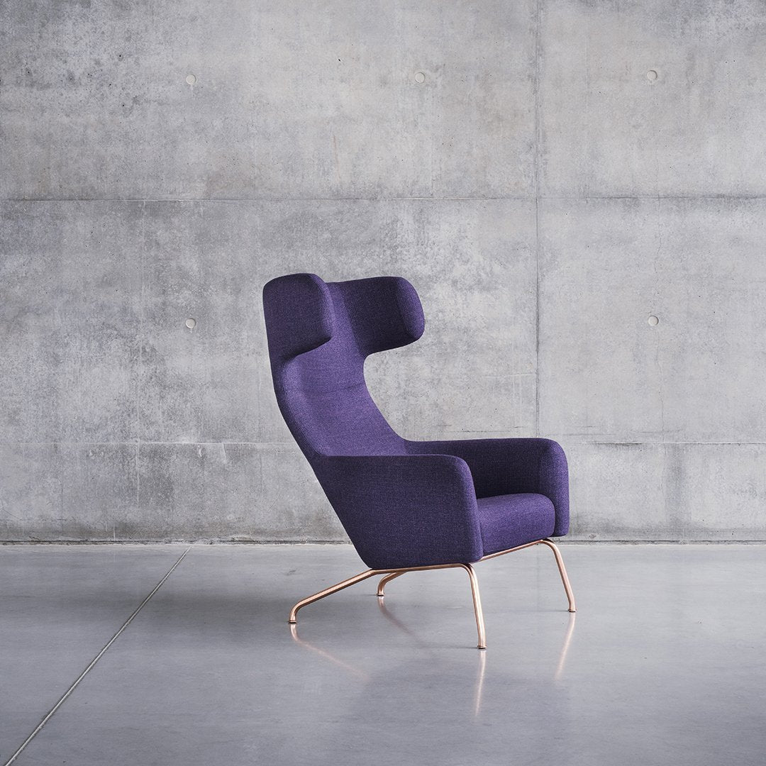 Modern purple upholstered chair with a sleek design and rose gold legs, set against a gray concrete backdrop.