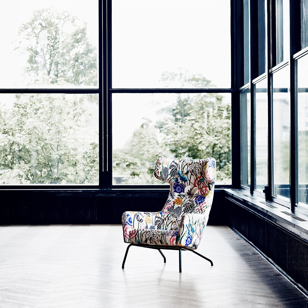 Colorful floral armchair with intricate patterns, featuring a vibrant mix of blues, reds, and greens in a modern setting.