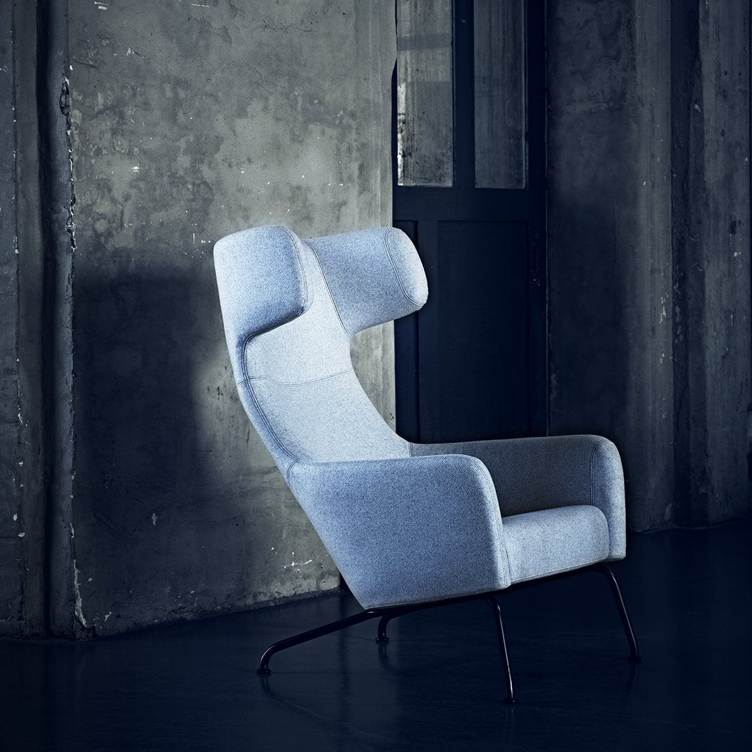 Light gray upholstered armchair with a modern design, featuring soft curves and a textured finish against a dark background.