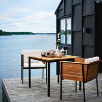 Elegant wooden dining table with black metal accents and creamy white cushions, set against a serene lake backdrop.