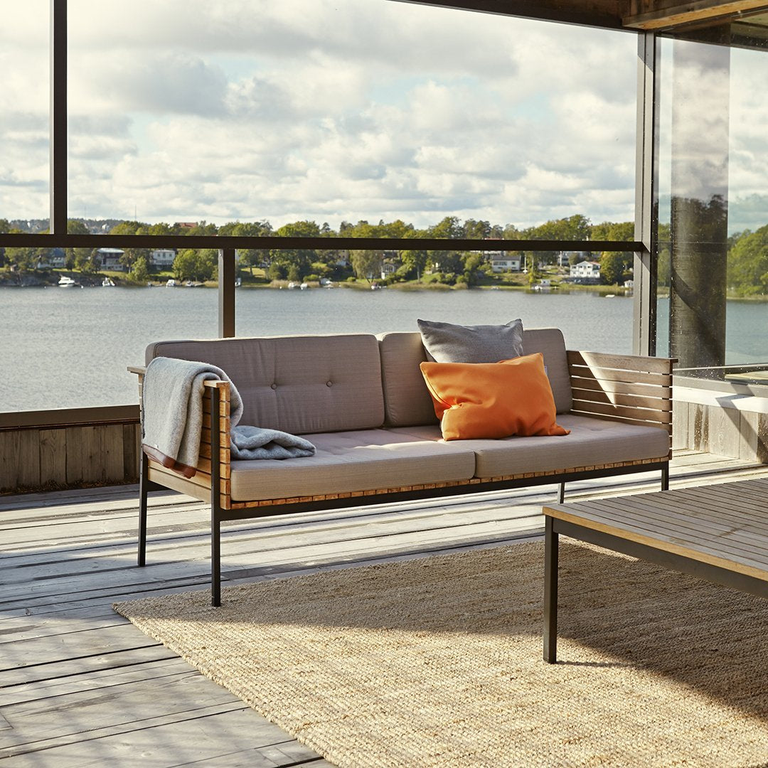 Light gray outdoor sofa with orange accent pillows, subtle textures, and natural wood tones against a scenic backdrop.