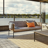 Light gray outdoor sofa with orange accent pillows, subtle textures, and natural wood tones against a scenic backdrop.