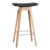 Black cushioned seat with natural wood legs and silver footrest, featuring a sleek, minimalist design.
